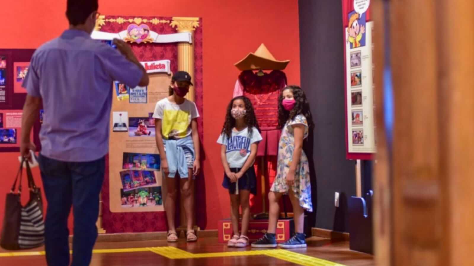 Homem tirando foto de três meninas em exposição de arte