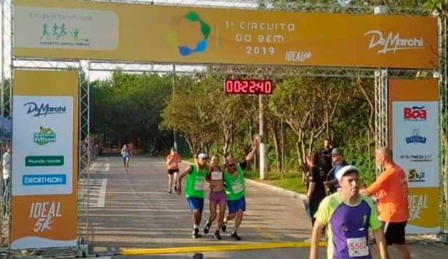 Moradores em sitação de rua praticantes de corrida cruzando linha de chegada com corredora apoiada em seus braços