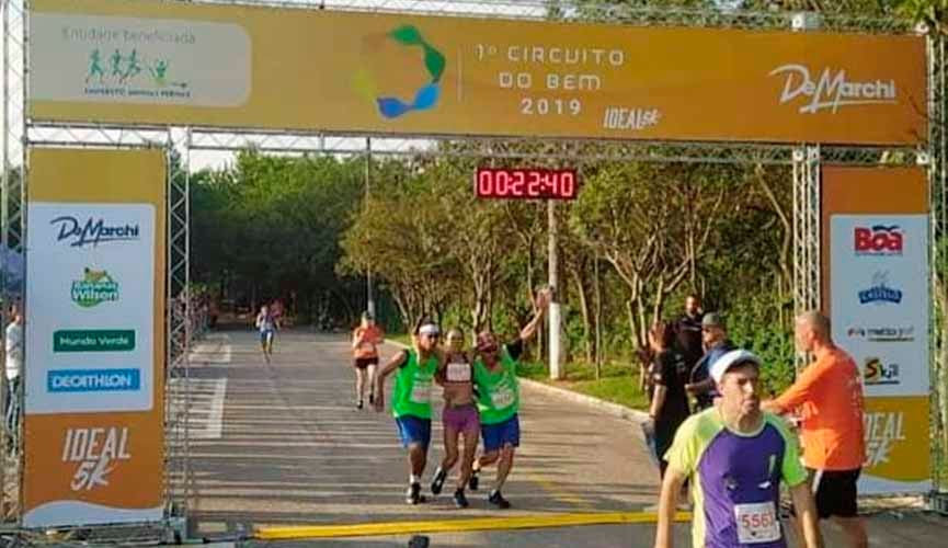 Moradores em sitação de rua praticantes de corrida cruzando linha de chegada com corredora apoiada em seus braços