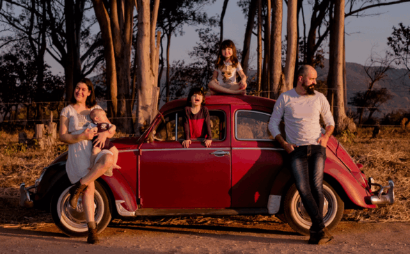 Kleber e esposa, Susana, com Caetano no colo estão encostados no carro. Olívia no teto e Emanuel na janela.