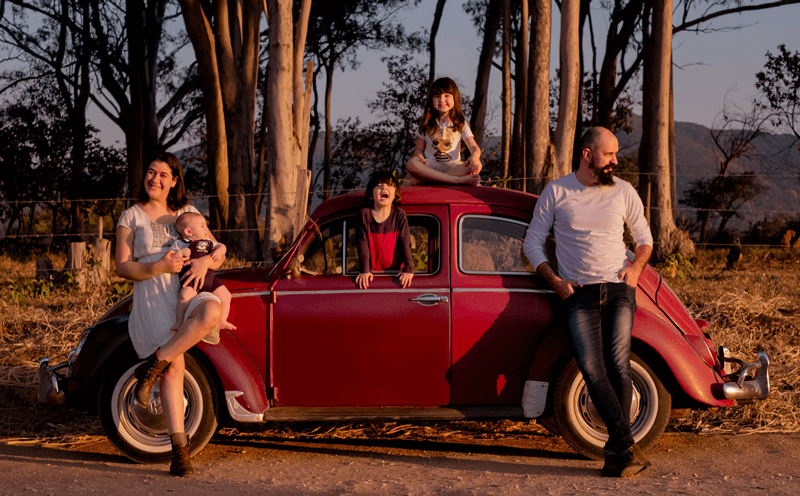 Kleber e esposa, Susana, com Caetano no colo estão encostados no carro. Olívia no teto e Emanuel na janela.