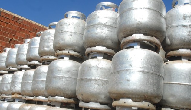 Botijões de gás de cozinha empilhados em fileira ao lado de muro de tijolos