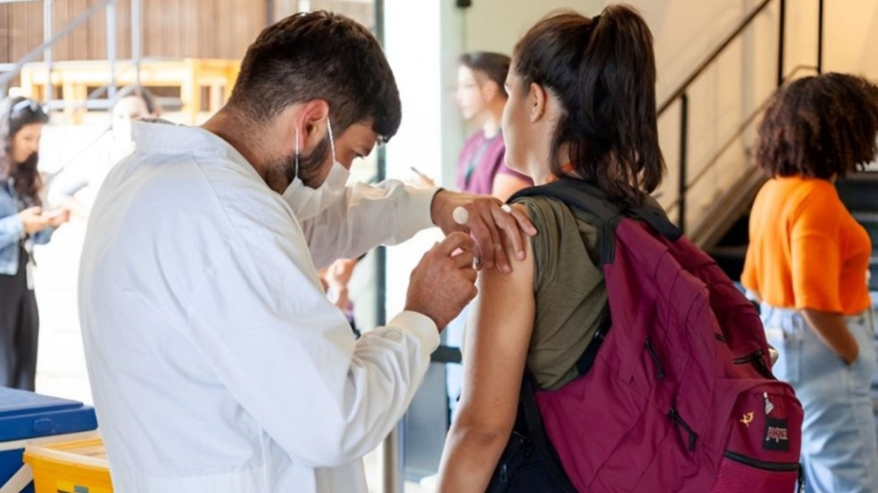 Homem aplicando vacina em estudante