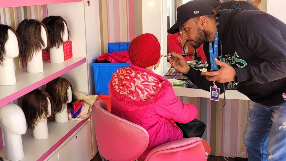 Profissional maquiador atende paciente oncológica usando lenço vermelho, em espaço com prateleiras cheias de perucas da ONG Cabelegria. Profissional maquiador atende paciente oncológica usando lenço vermelho, em espaço com prateleiras cheias de perucas da ONG Cabelegria.