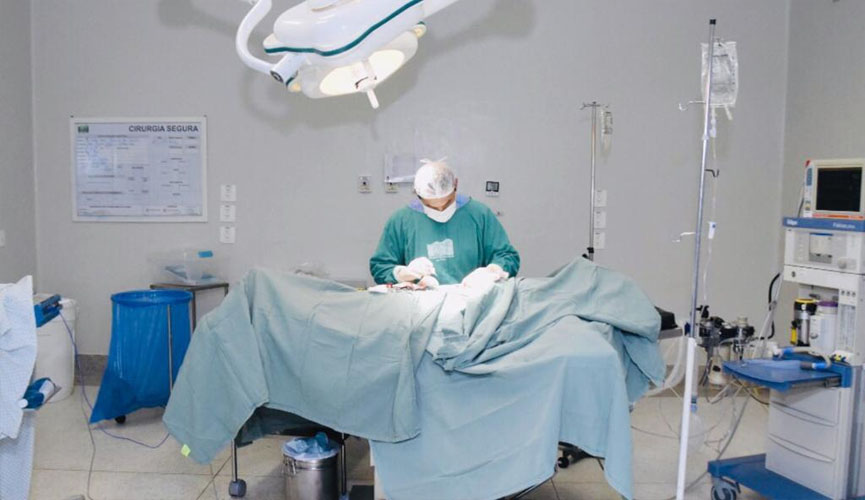 cirurgião em centro cirúrgico com paciente em maca coberto por lençol