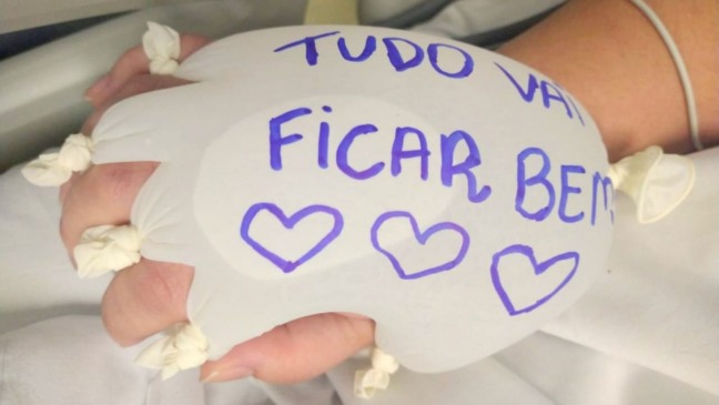 Mão de paciente com luva com água, com o escrito "Tudo vai ficar bem"