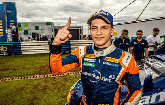 Guilherme faz número 1 com o dedo indicador em frente ao carro da corrida