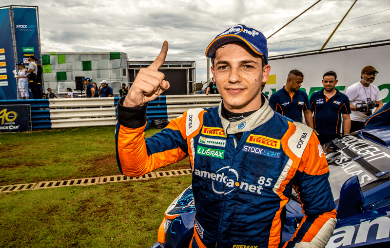 Guilherme faz número 1 com o dedo indicador em frente ao carro da corrida