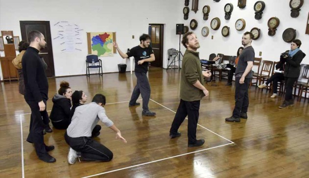 pessoas em oficina de dança, com 7 pessoas dentro de um quadrado, sendo duas à frente, três ao meio agaixadas e duas ao fundo. Outras pessoas observam à frente