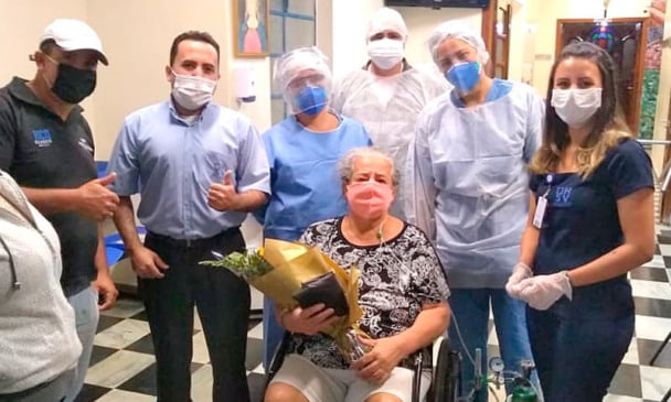 Paciente em cadeira de rodas, com buquê de flores, com pessoas ao lado