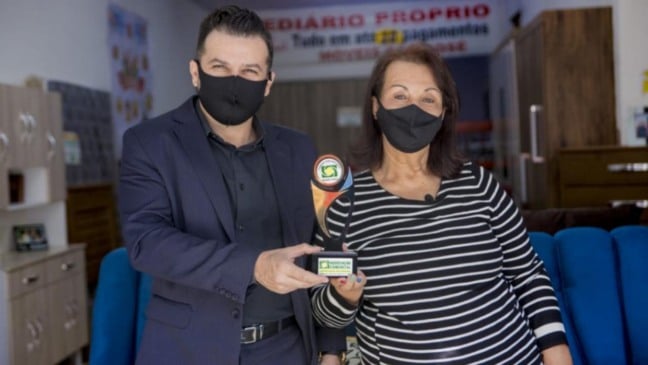 Mark William Ormenese Monteiro, entregando a Aiche um troféu personalizado do projeto em homenagem à história da loja