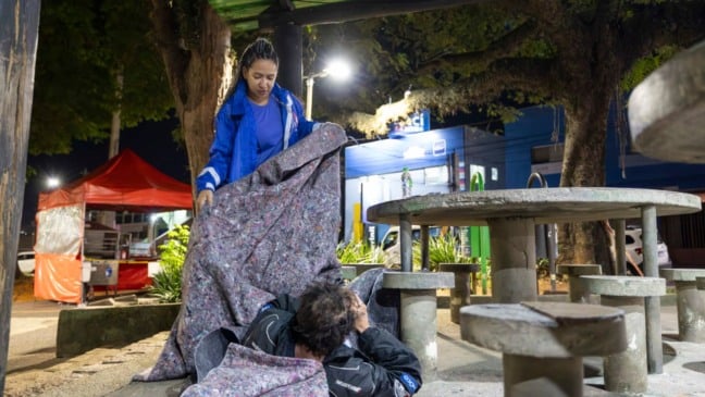 Mulher cobrindo homem em situação de rua