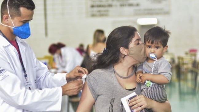 Mulher com bebê no colo, sendo vacinada em Jundiaí