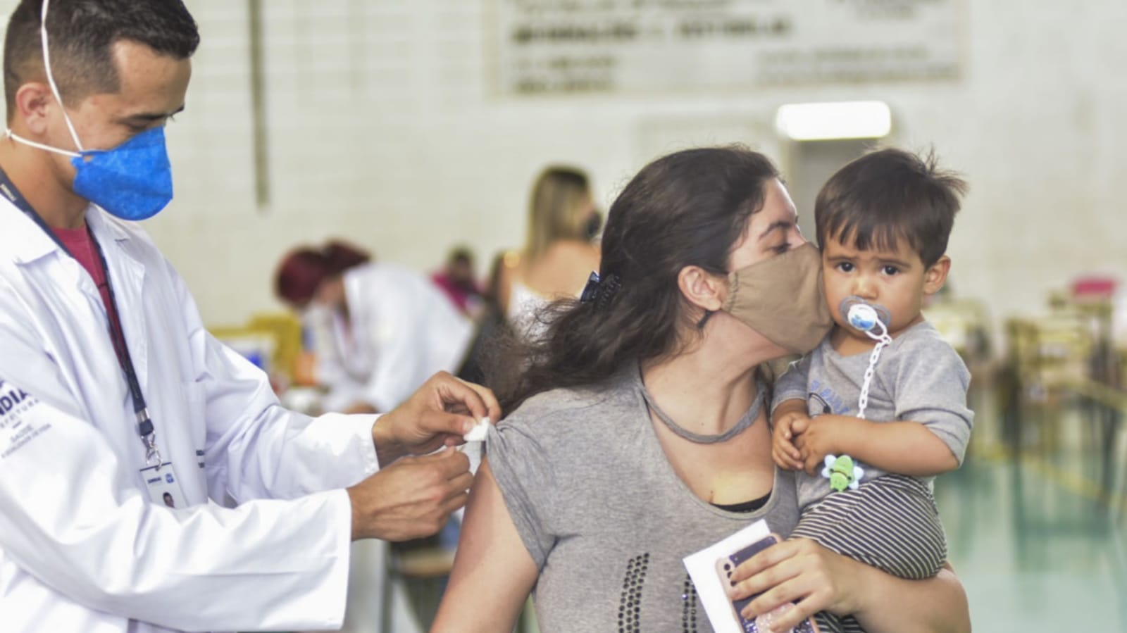 Mulher com bebê no colo, sendo vacinada em Jundiaí