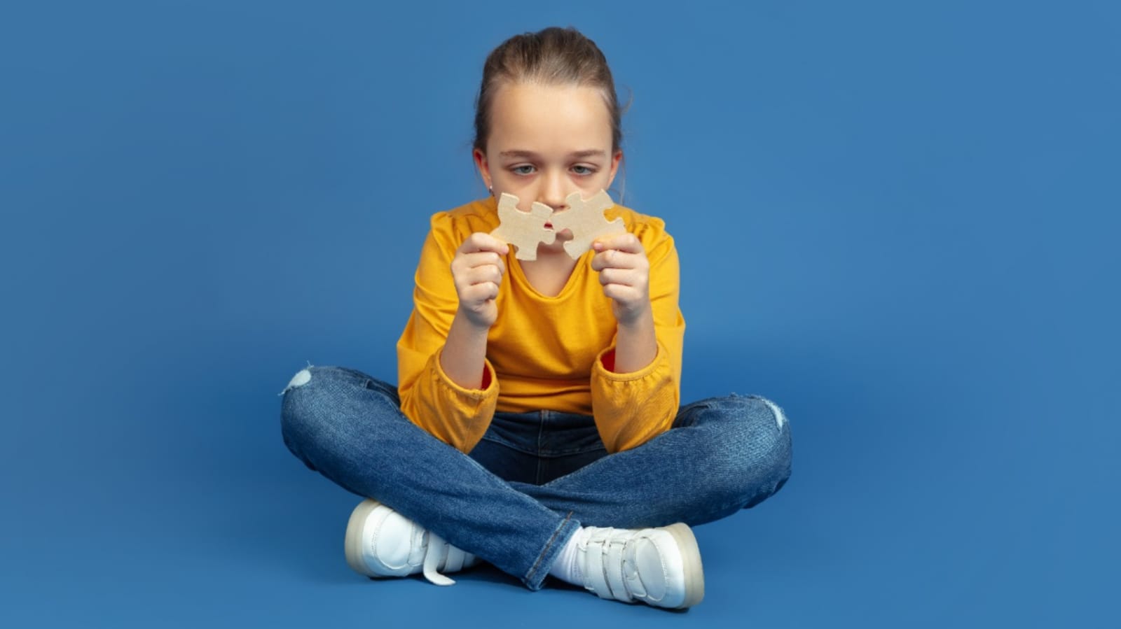 Criança com peças de quebra-cabeça nas mãos sentada em fundo azul