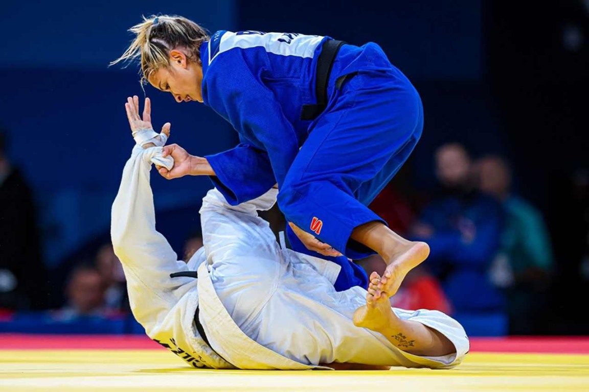 Judoca brasileira em ação durante luta nos Jogos Olímpicos de Paris 2024, vestindo kimono azul, aplicando técnica em adversária.