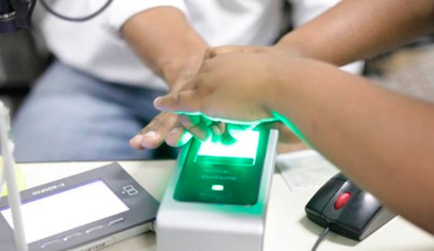 imagem mostra pessoa cadastrando a biometria em máquina do TSE. a foto é focada em duas mãos: a da pessoa que está cadastrando e ado funcionáro que está colocando a mão da pessoa sobre o aparelho