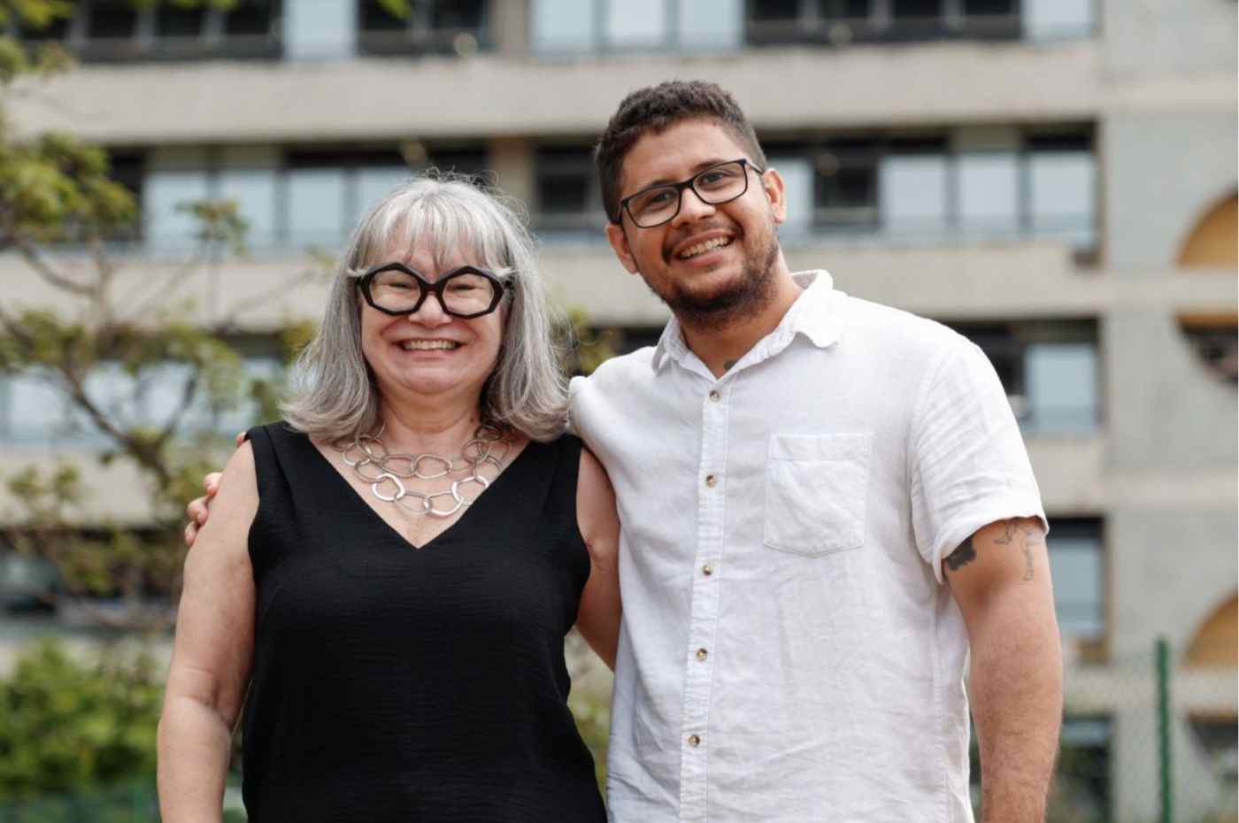 Dra. Márcia Facci assume a gestão da saúde em Jundiaí, sorrindo ao lado de Allan Gomes de Lorena, em ambiente externo com prédio ao fundo