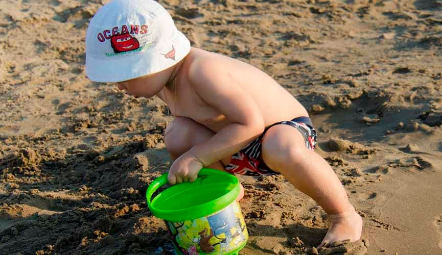 criança na praia brincando na areia com baldinho