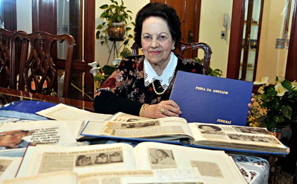 Imagem de Mercedes Ladeira Marchi, fundadora da Feira da Amizade, segurando um álbum azul com o título "Feira da Amizade Jundiaí