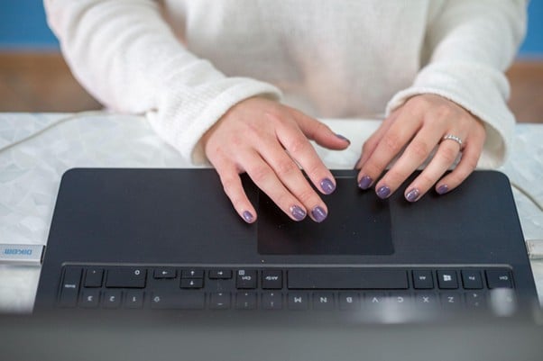 Usuária digitando em um notebook Multilaser Legacy com unhas pintadas de roxo, vestindo um suéter branco, em ambiente iluminado.