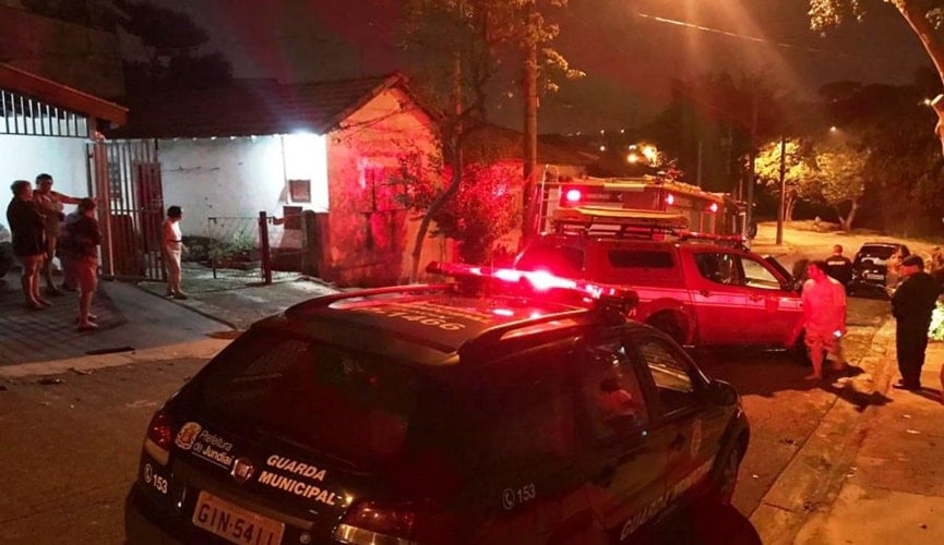 Foto da viatura da Guarda Municipal de Jundiaí, ao lado do caminhão do Corpo de Bombeiros, em uma rua com pessoas em torno de uma casa.