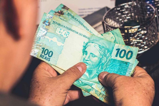 Pessoa segurando notas de R$ 100 reais brasileiros
