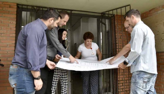 técnicos seguram mapa de projeto de unidade básica de saúde que será reformada
