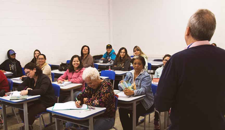 sala de aula com alunos da Educação de Jovens e Adultos, com professor de costa à frente e os alunos sentados ao fundo