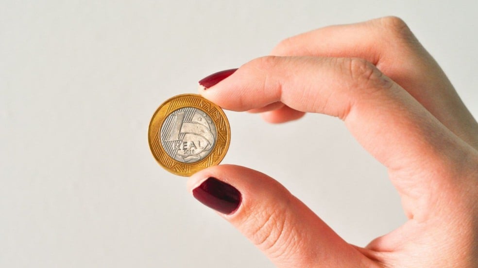Mulher segurando moeda de R$ 1