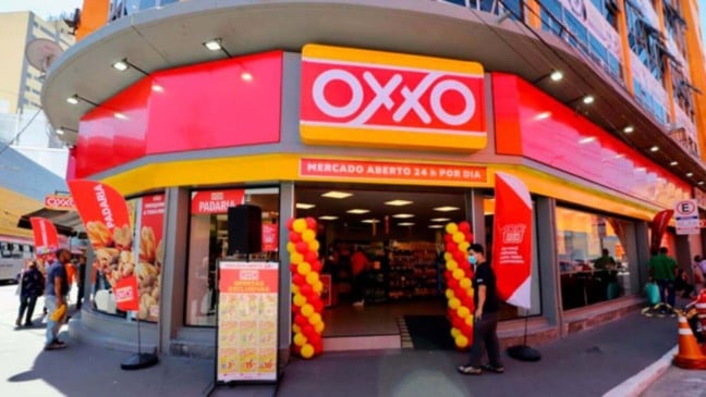 Fachada da loja OXXO em Jundiaí com letreiro vermelho e amarelo, entrada decorada e pessoas passando em frente. Fachada da loja OXXO em Jundiaí com letreiro vermelho e amarelo, entrada decorada e pessoas passando em frente.