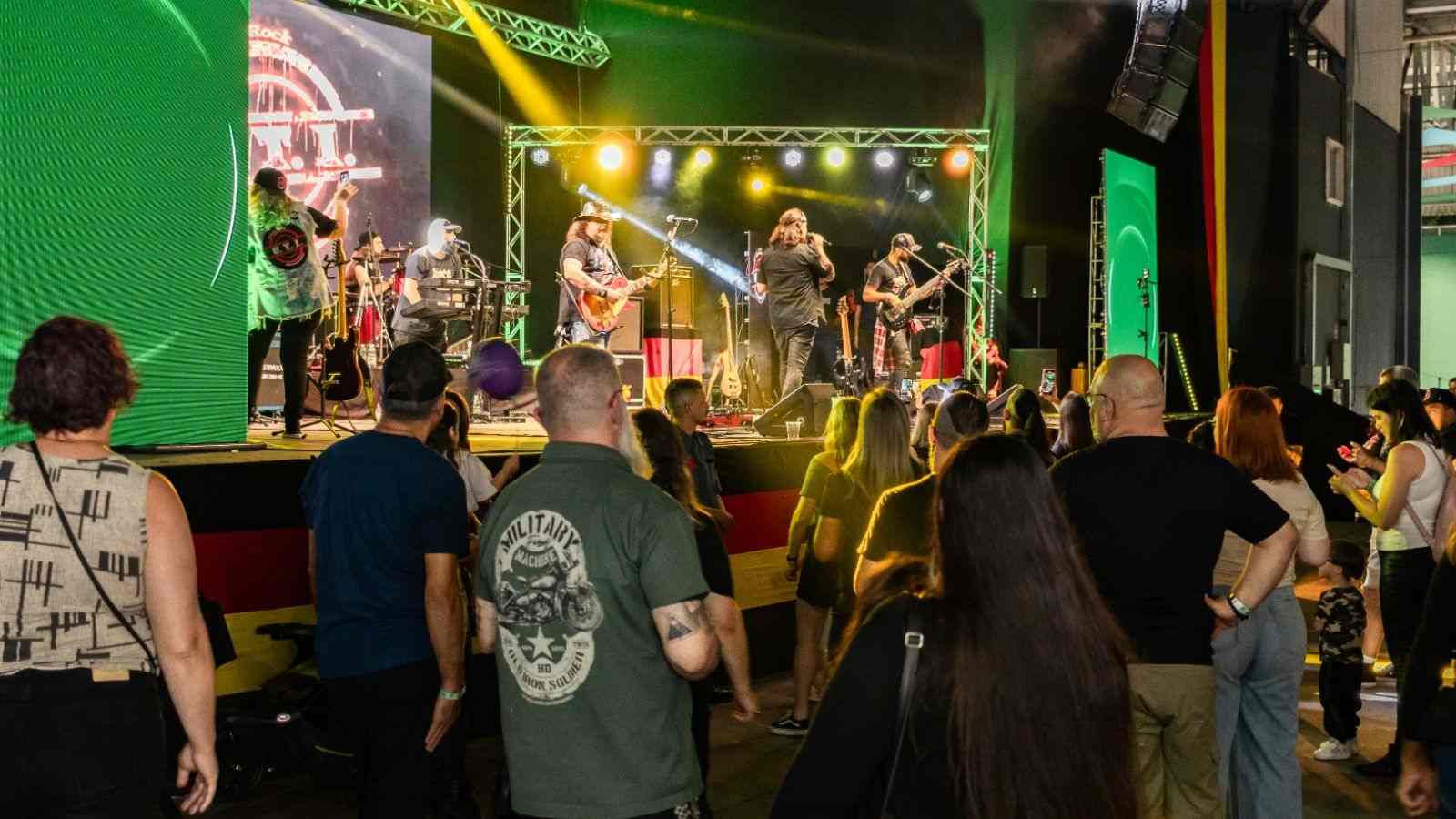 Pessoas assistem a uma banda de rock se apresentando no palco da Oktober Polo Jundiaí, no Parque da Uva, com luzes coloridas e público animado.