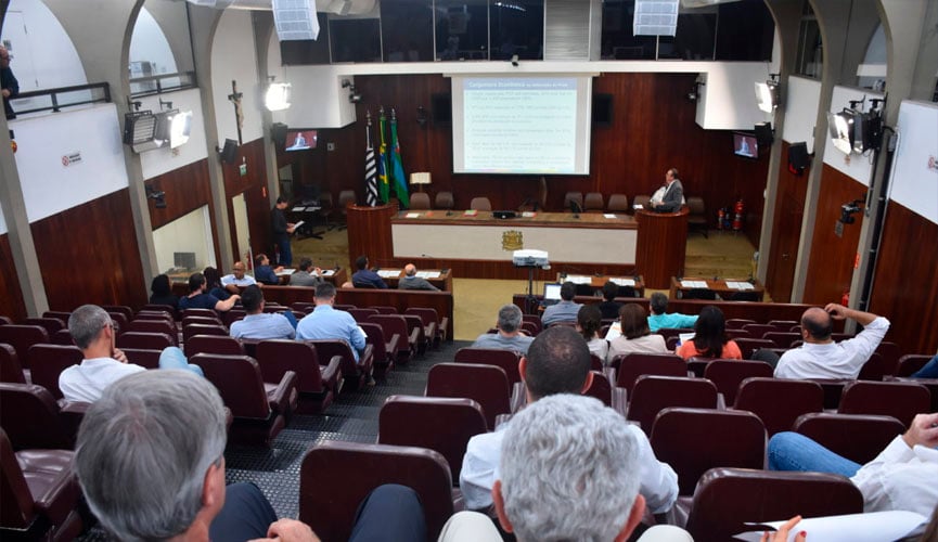 pÚBLICO SENTADO EM CADEIRAS DE CÂMARA MUNICIPAL ACOMPANHANDO AUDIÊNCIA PÚBLICA COM HOMENS SENTADOS À FRENTE pÚBLICO SENTADO EM CADEIRAS DE CÂMARA MUNICIPAL ACOMPANHANDO AUDIÊNCIA PÚBLICA COM HOMENS SENTADOS À FRENTE