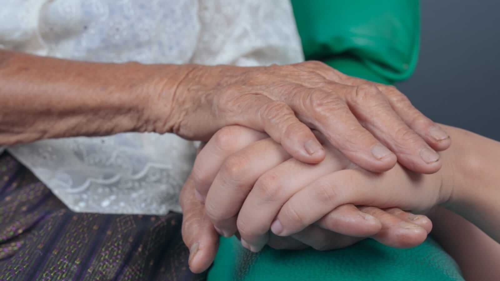 Idosa segurando mão de jovem