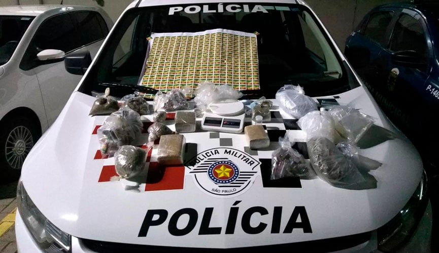 capô de carro da polícia com 2,398 quilos de maconha, um galão de 10 litros de lança-perfume, uma balança de precisão, uma tábua para corte da droga, uma faca, diversas embalagens vazias e R$ 268