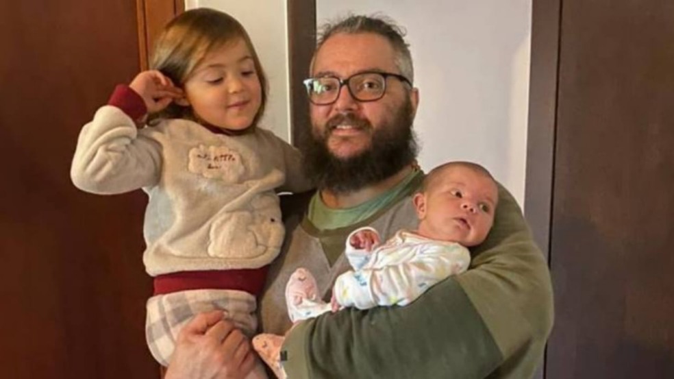 Homem com as duas filhas no colo