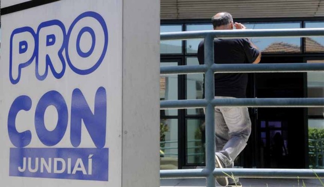 Metade da foto mostra muro em frente ao procon jundiaí com os dizeres "Procon Jundiaí". Outra metade mostra, ao fundo, homem adentrando o local