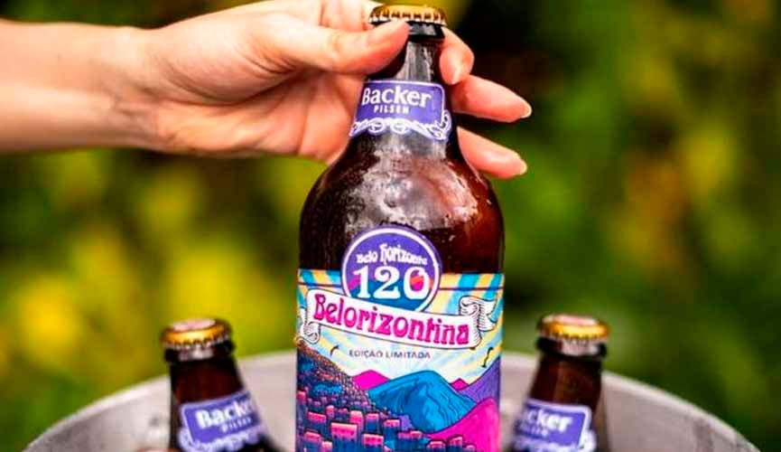 mão de mulher segura cerveja belorizontina em balde com gelo. essa cerveja está mais acima. dentro do balde, há outras duas cervejas da mesma marca