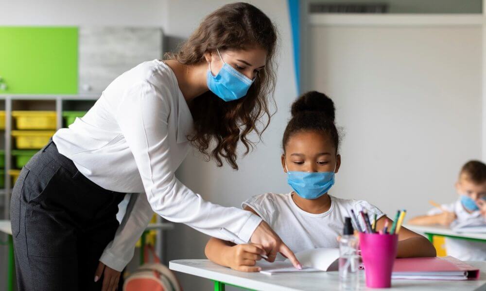 Professor com aluna de máscaras em sala de aula