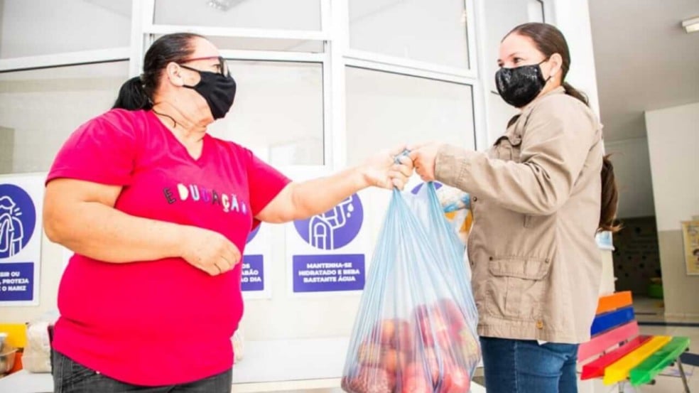 Mulher entrega sacola de frutas para outra