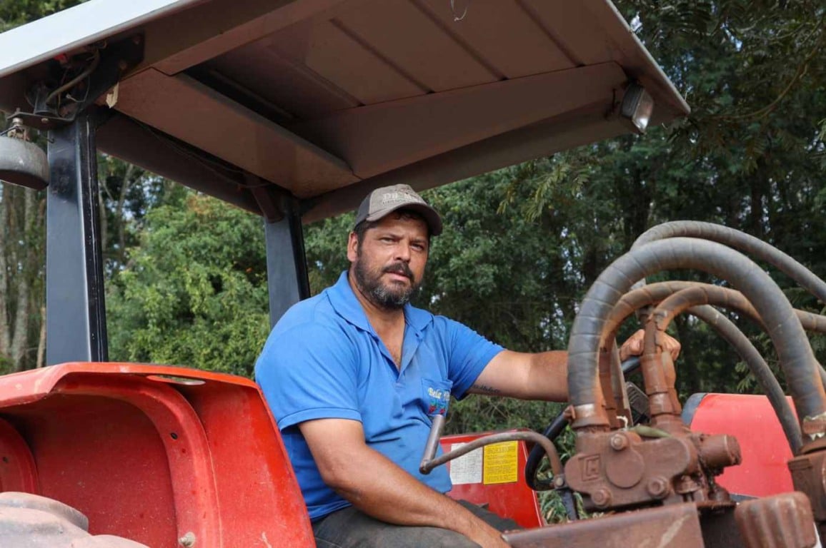 Produtor rural operando um trator vermelho em meio a uma área arborizada