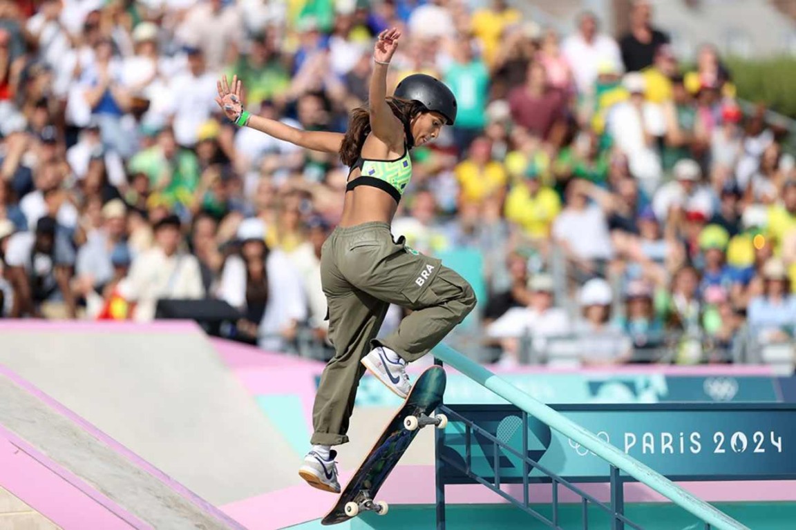 Skatista brasileira competindo nos Jogos Olímpicos de Paris 2024, realizando manobra em pista de skate, com público ao fundo.