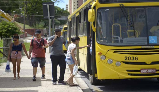 ônibus amarelo de jundiaí parado em avenida enquanto pessoas que estão na calçada paradas no ponto de ônibus sobem para dentro dele