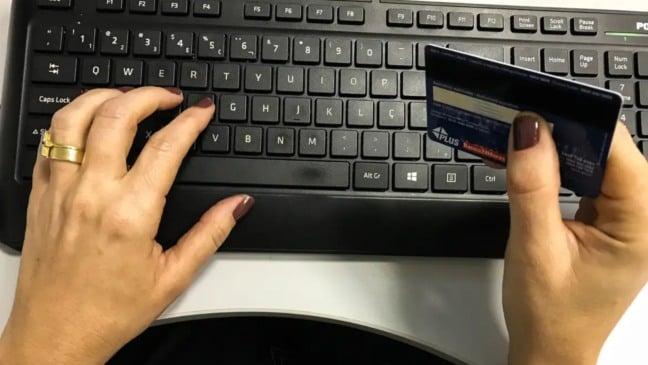 Mão de mulher segurando um cartão sobre um teclado - Receita Federal