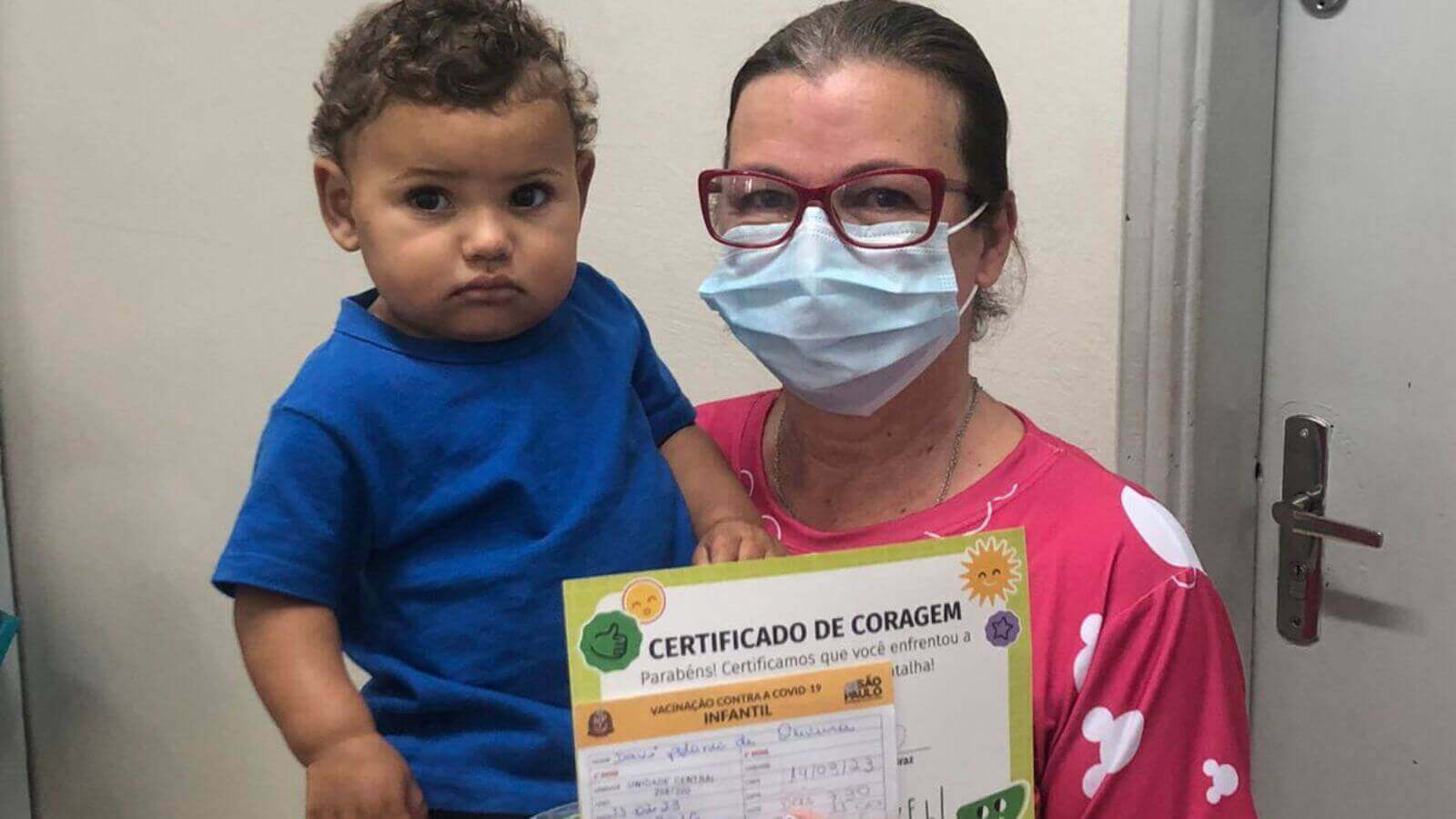 Mulher com bebê no colo e carteira de vacinação contra Covid