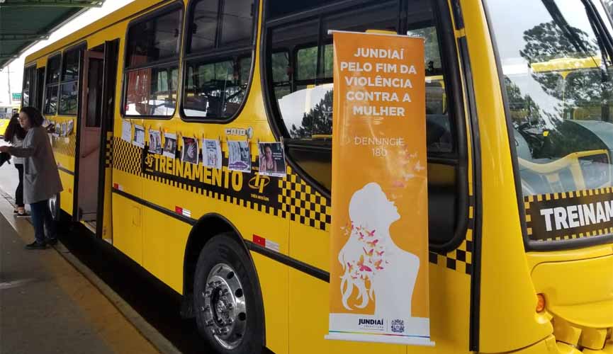Ônibus urbano de Jundiaí em campanha contra violência a mulher, com banner "Jundiaí pela fim da violência contra a mulher, denuncie 180". Mais atrás, também na lateral da parte externa do ônibus, imagens de conscientização formal um varal de fotos Ônibus urbano de Jundiaí em campanha contra violência a mulher, com banner "Jundiaí pela fim da violência contra a mulher, denuncie 180". Mais atrás, também na lateral da parte externa do ônibus, imagens de conscientização formal um varal de fotos