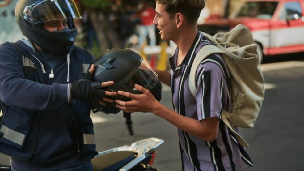 Motociclista dando capacete para passageiro