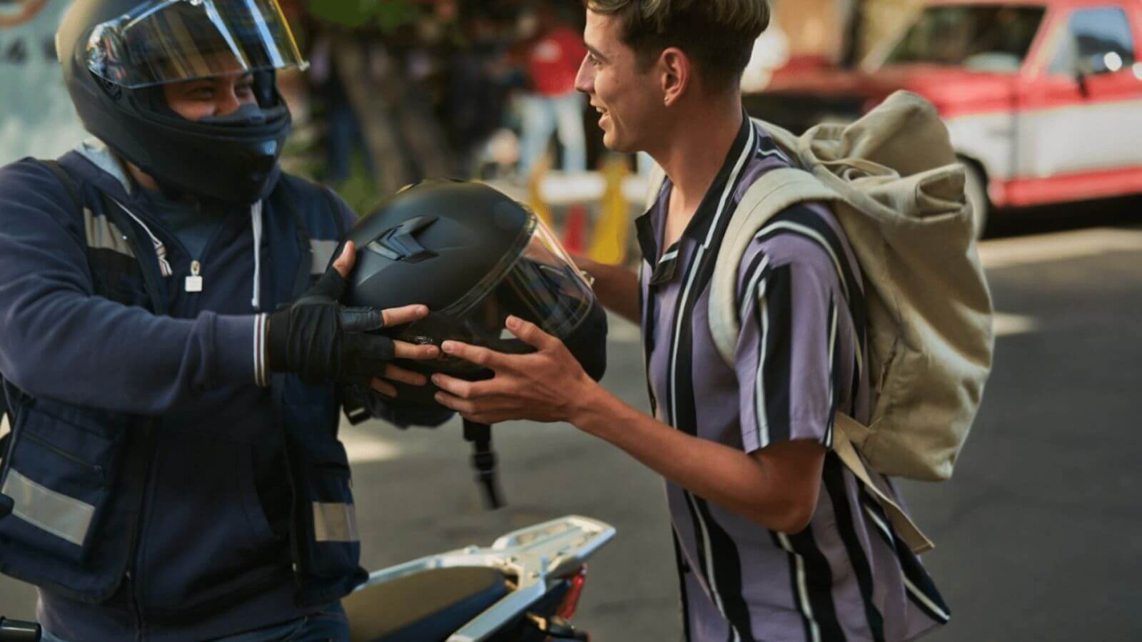 Motociclista dando capacete para passageiro