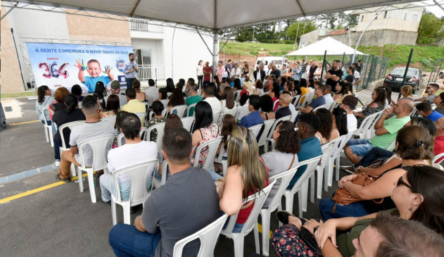 Pessoas sentadas em cadeiras plásticas acompanham solenidade de entrega das chaves do residencial caméia. evento é dentro do condomínio