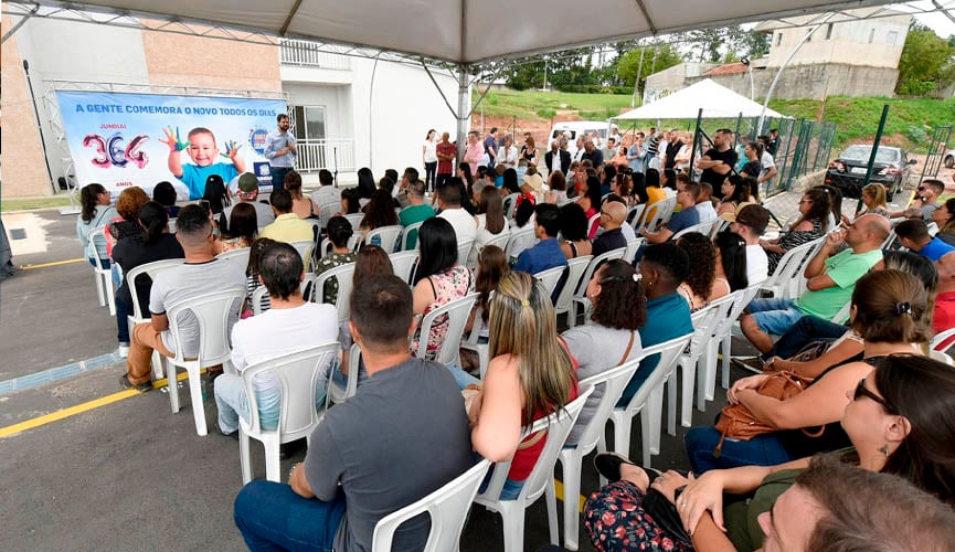 Pessoas sentadas em cadeiras plásticas acompanham solenidade de entrega das chaves do residencial caméia. evento é dentro do condomínio